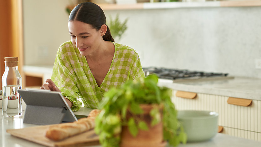 A woman uses a Surface device while sitting in a kitchen.